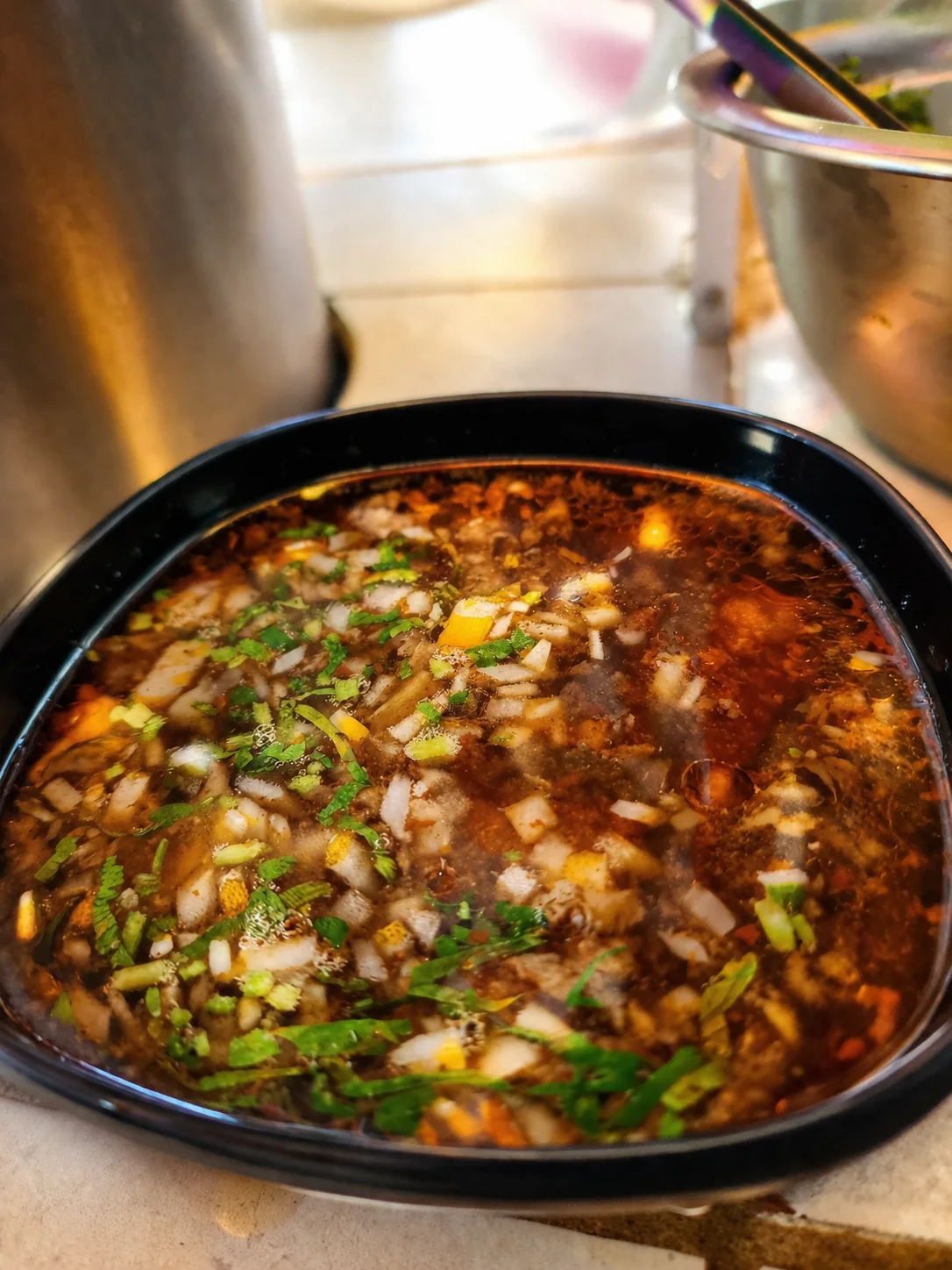 Fotografía gastronómica en primer plano de consomé de birria servido en un tazón negro