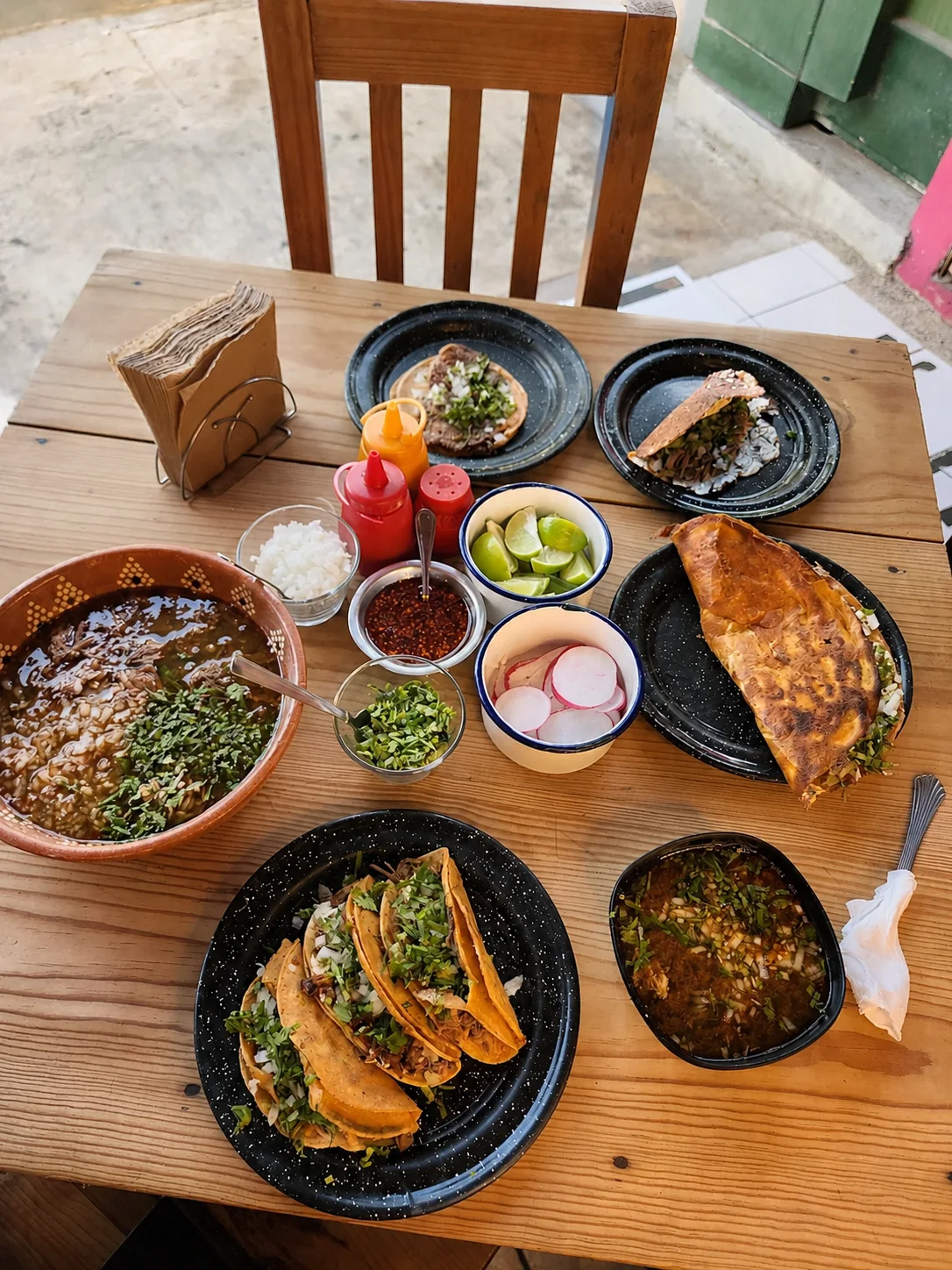 Fotografía cenital de la mesa completa de Birriería El Norteño con tacos y consomé
