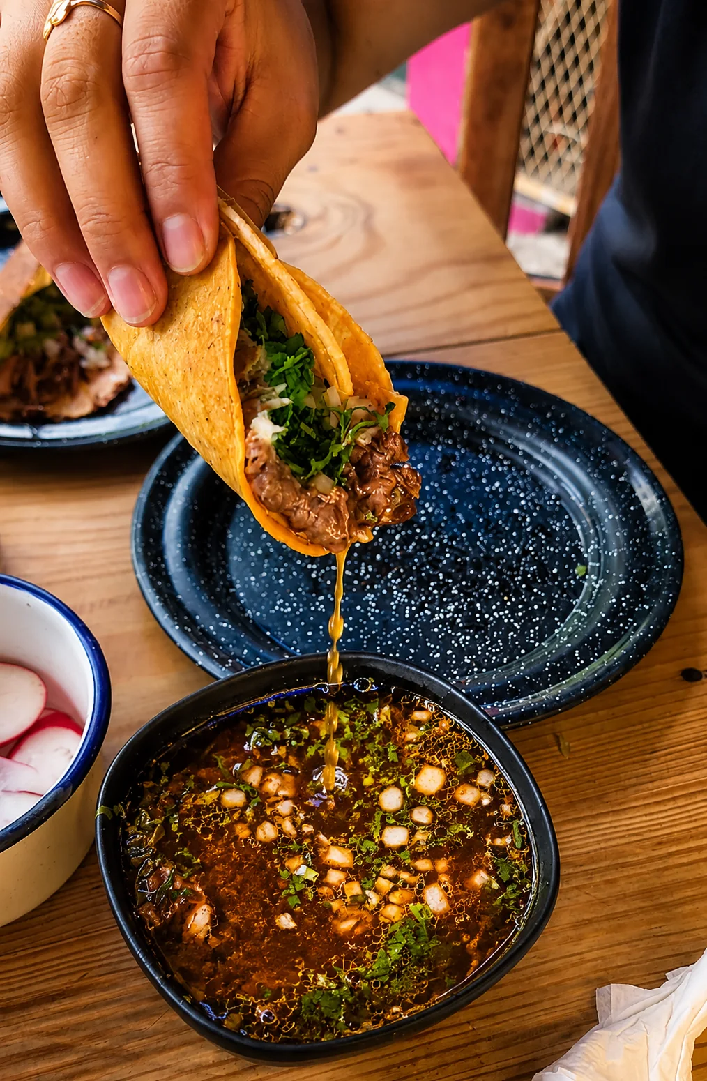 Fotografía de acción de un taco de birria sumergiéndose en consomé